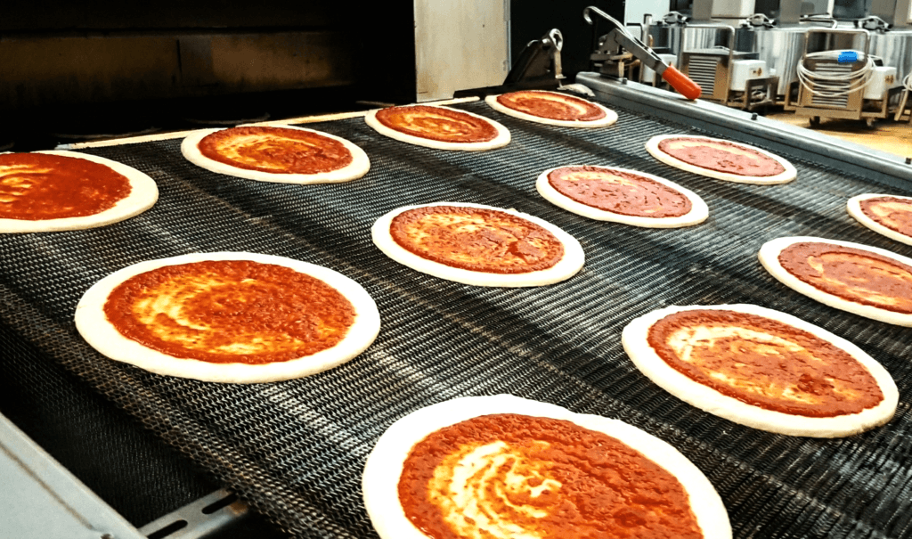 High-speed industrial pizza production line showing mechanical rounding and hot pressing processes.